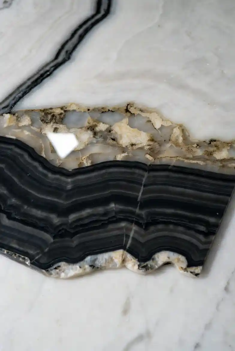 Tranche d'onyx noir poli aux veines blanches naturelles, posée sur une surface en marbre de luxe, décoration minérale Gemska Maroc."